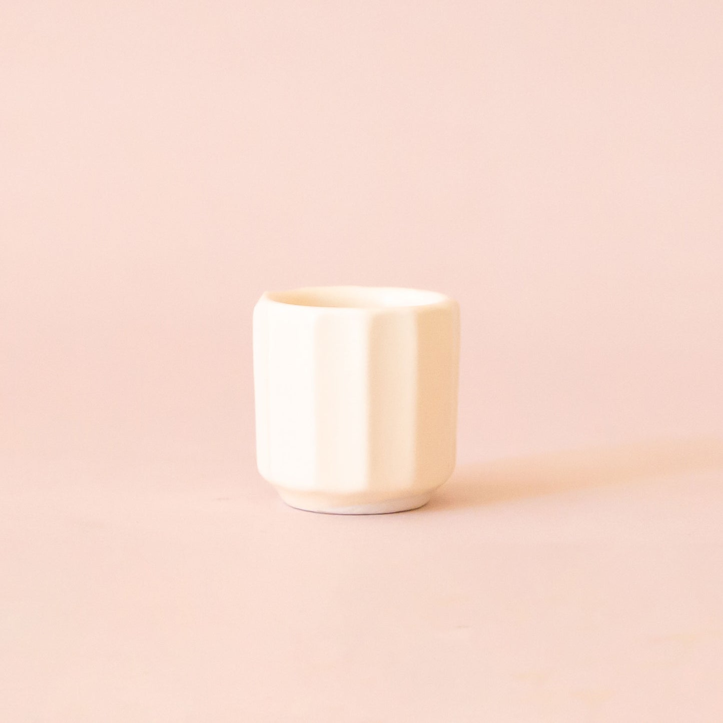 An itty bitty pot about the size of thimble that is a white color sits in the middle of a page. The background is a soft pink color.