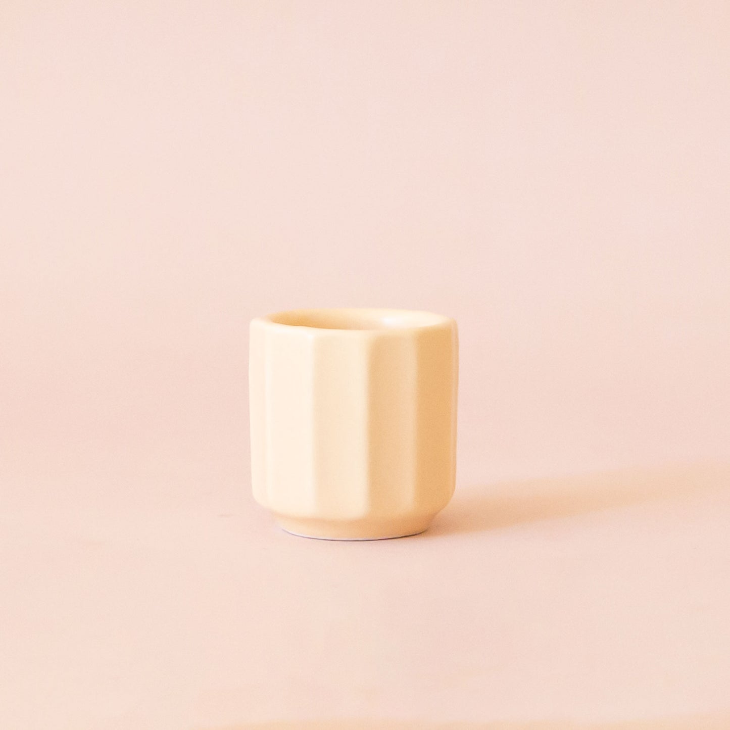 An itty bitty pot about the size of thimble that is a soft beige color sits in the middle of a page. The background is all a soft white color.