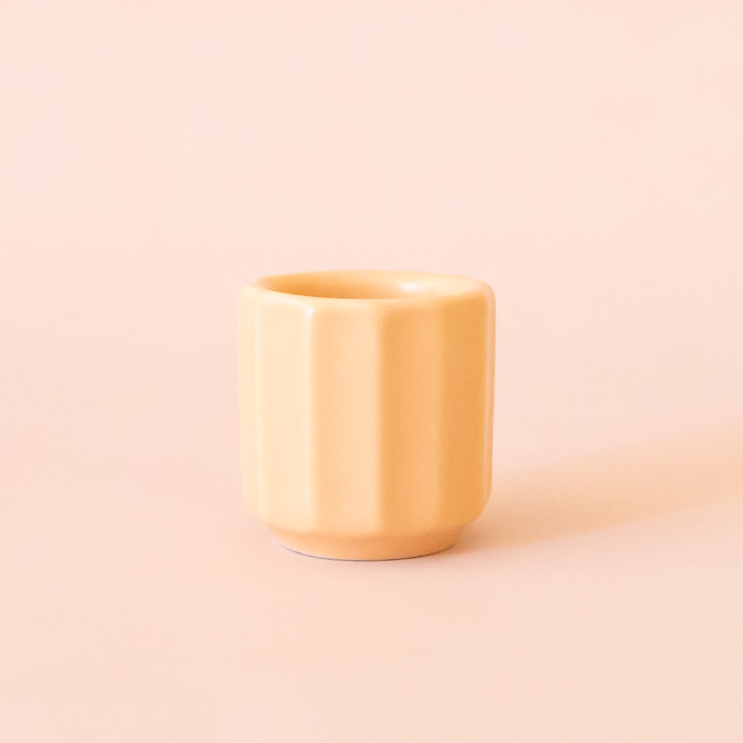 An itty bitty pot about the size of thimble that is a soft peach color sits in the middle of page. The tiny pot has little ridges all around it. The background is all a soft white color.