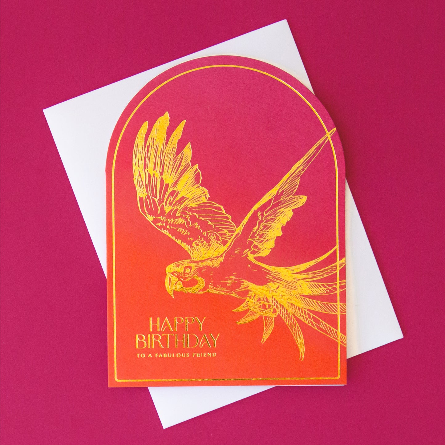 A hot pink and orange ombre colored arched shaped card with gold foiled text that reads, "Happy Birthday To A Fabulous Friend" along with a gold foiled parrot illustration.