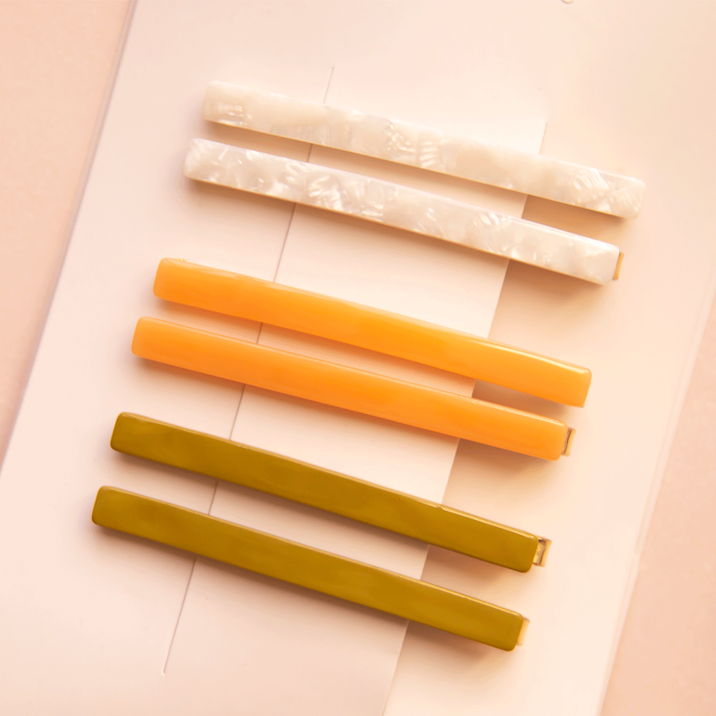 On a white packaging is six bobby pin clips in three different colors. From top to bottom is an ivory shell shade, mango orange, and olive green shade.