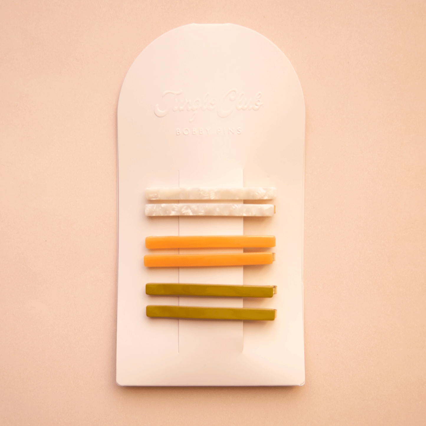 On a white packaging is six bobby pin clips in three different colors. From top to bottom is an ivory shell shade, mango orange, and olive green shade.