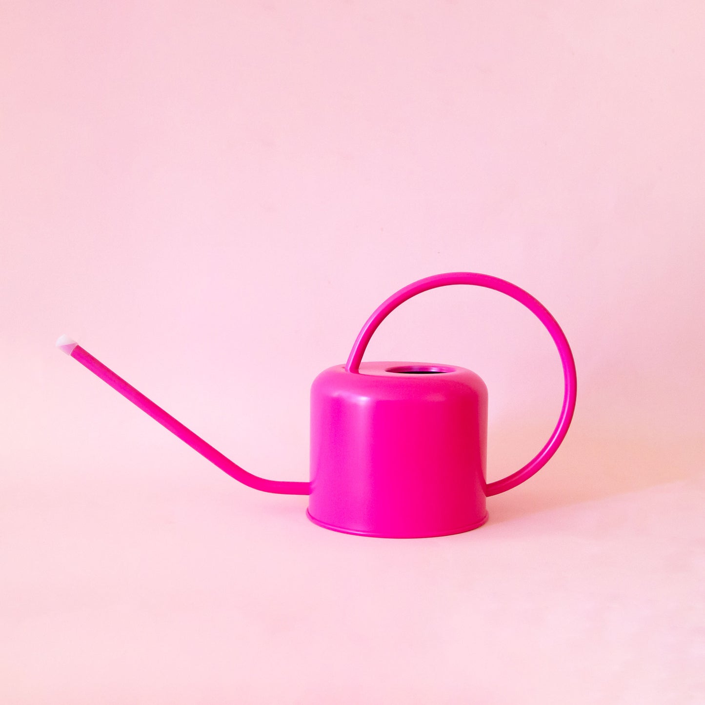 A hot pink metal watering can with a rounded handle and a long spout.