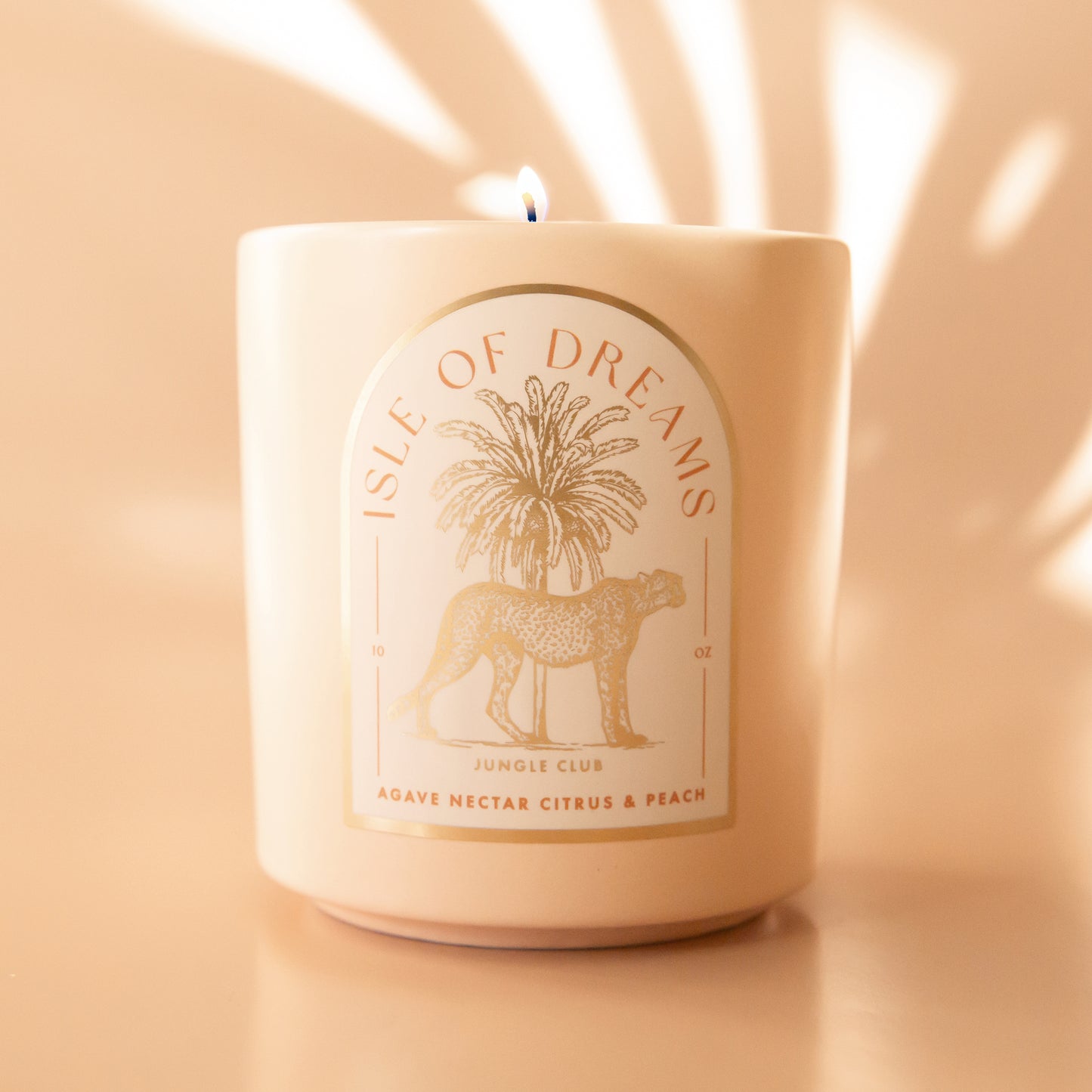 A neutral candle with an arched label with a cheetah and palm tree graphic and text that reads, 'Isle of Dreams'.