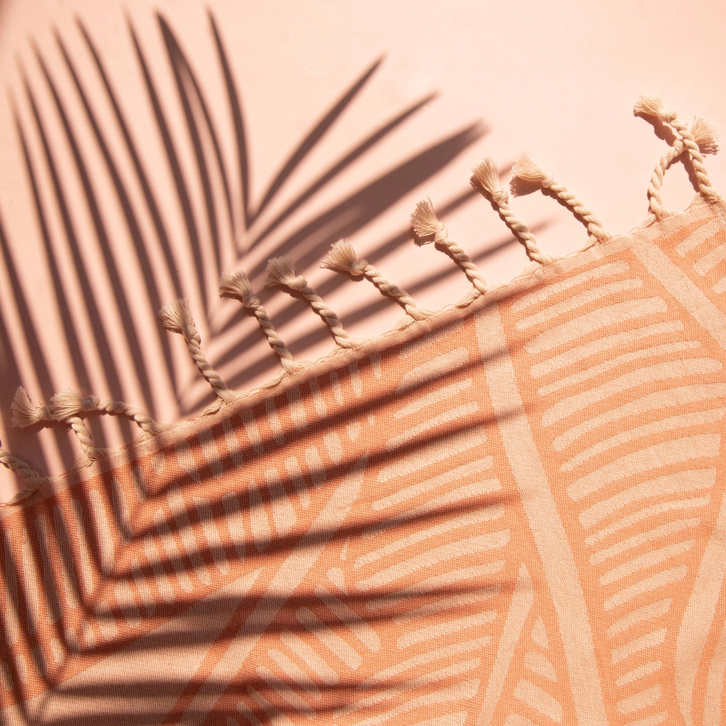 An orange beach towel with a banana leaf print and white tassels on each end.