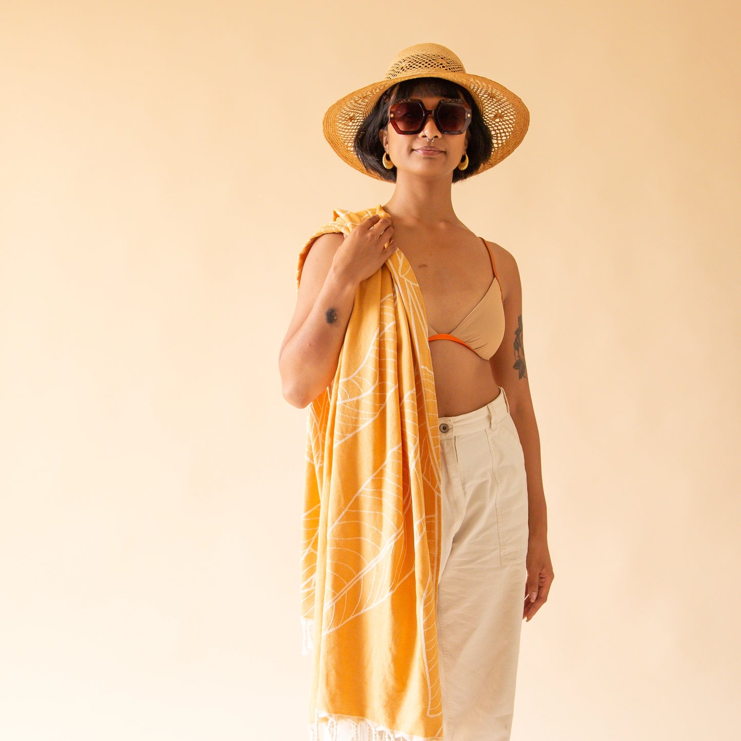 An orange beach towel with a banana leaf print and white tassels on each end.