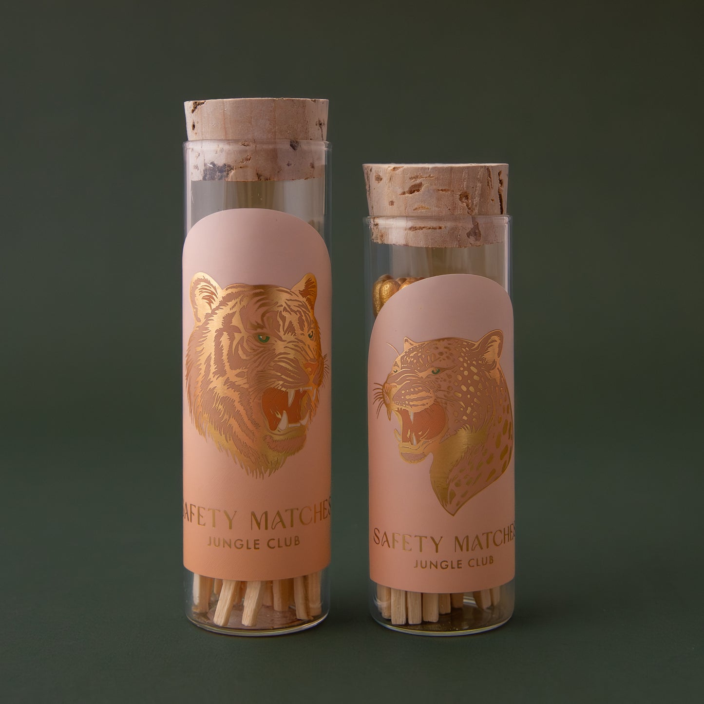 Two clear glass vials with a cork lid that contains wooden safety matches. The label on one of the vials has a gold foil leopard on it and the other is a gold foil tiger.
