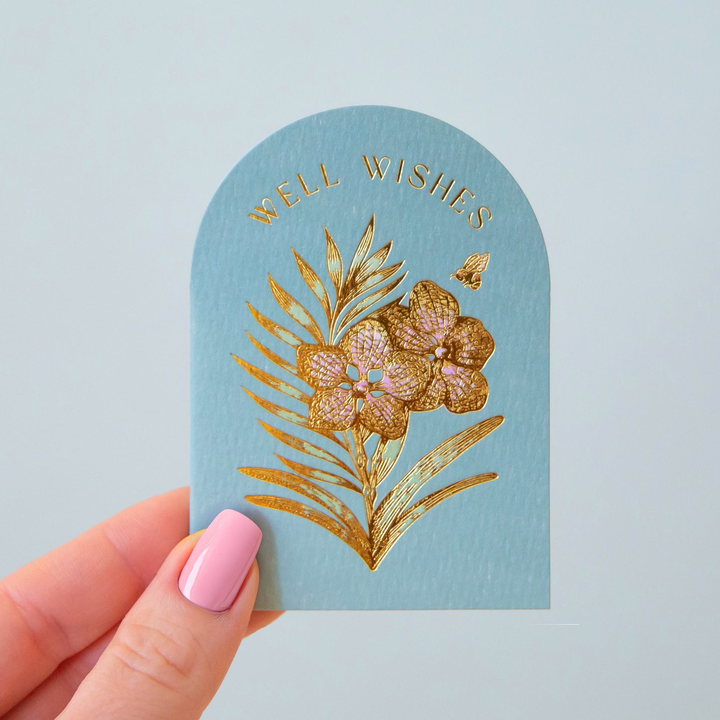 A light blue arched card with gold foiled text that reads, 'Well Wishes' and a flower design.