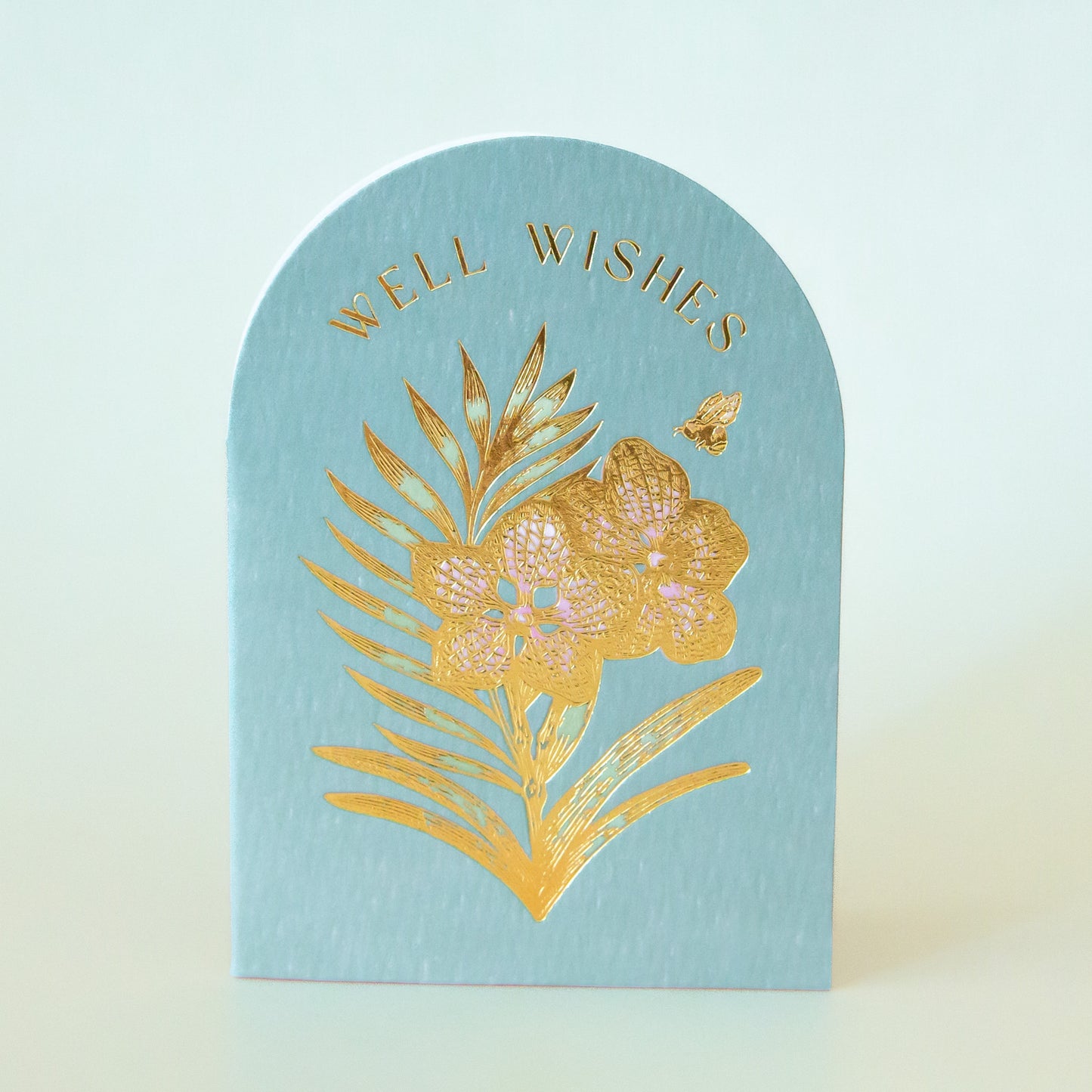 A light blue arched card with gold foiled text that reads, 'Well Wishes' and a flower design.