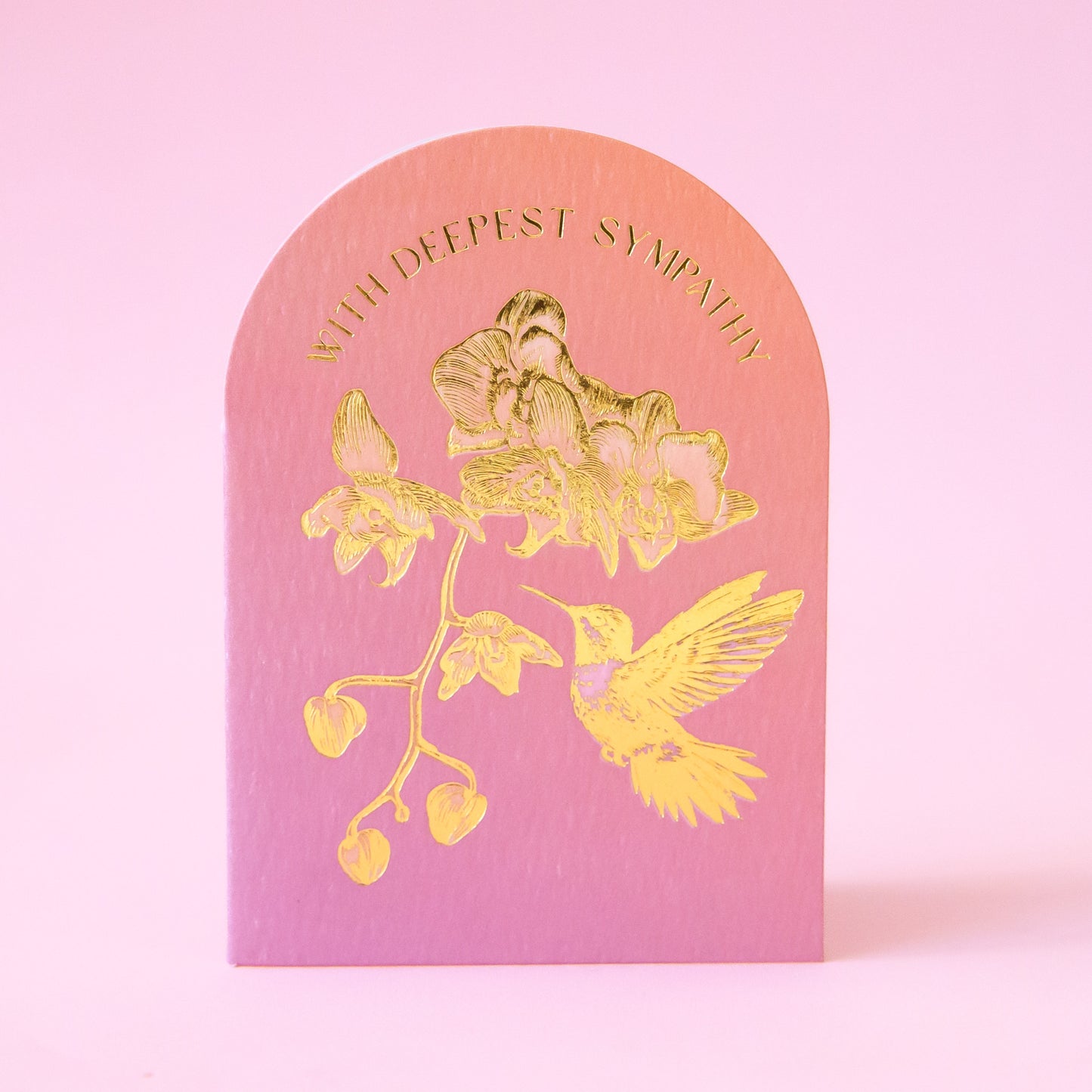 A light pink and orange card with gold foiled text and design of a hummingbird and flowers with text that reads, 'With Deepest Sympathy'.