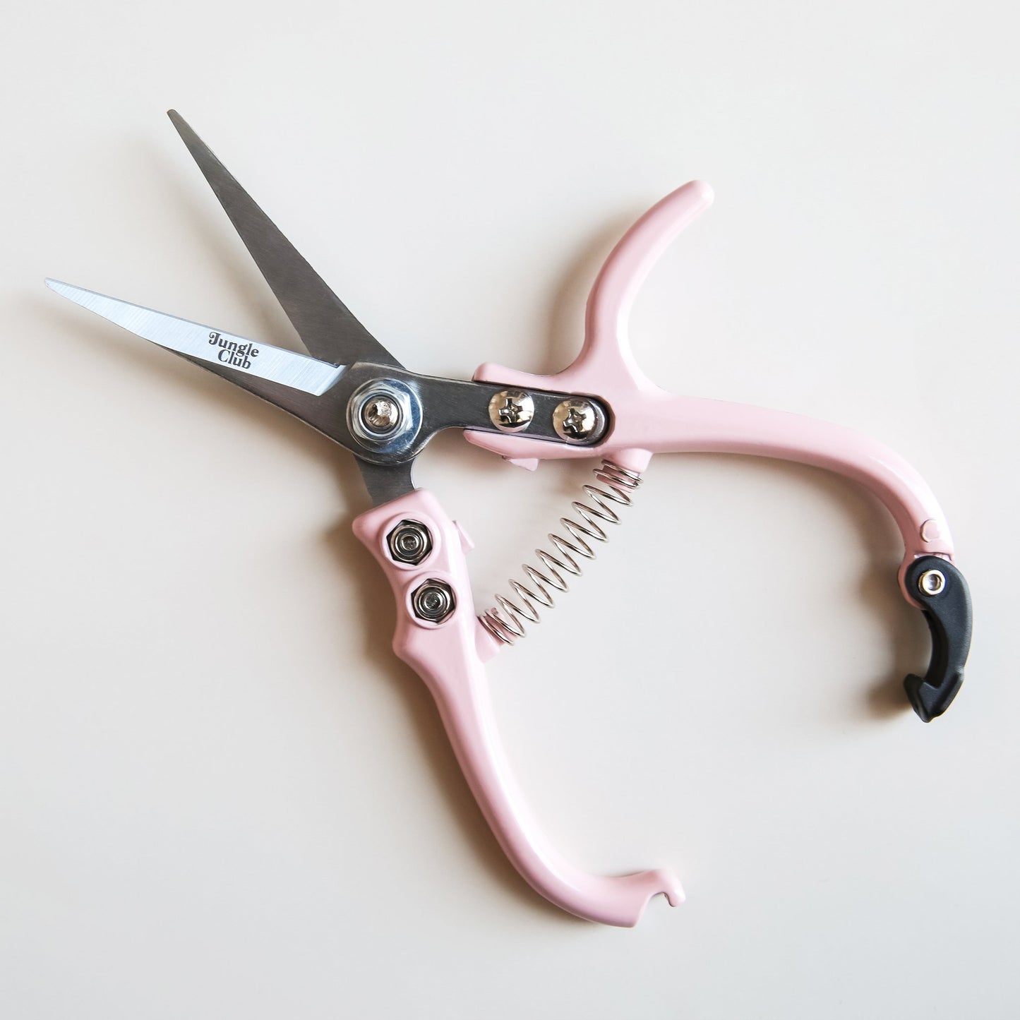 Pair of pruning shears with pastel pink handles and metal blades positioned open. The outer blade reads 'jungle club' in small, playful lettering. The back clasp of the shear handles remain unclipped, allowing for the shear blades to be open.