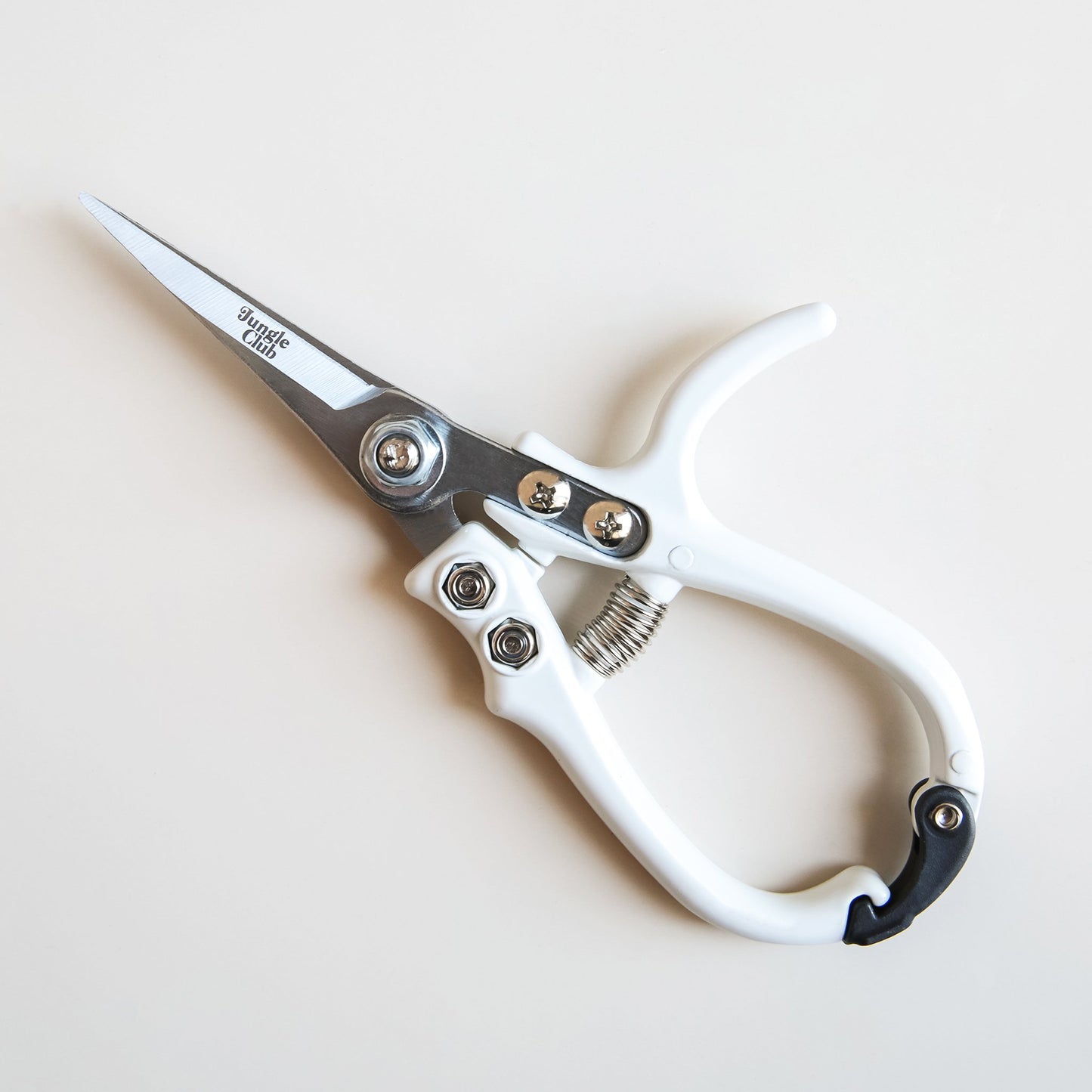 On a cream background is a white pair of pruning shears with silver metal and fixtures and small text on the metal part of the shears that reads, "Jungle Club" in small black letters.