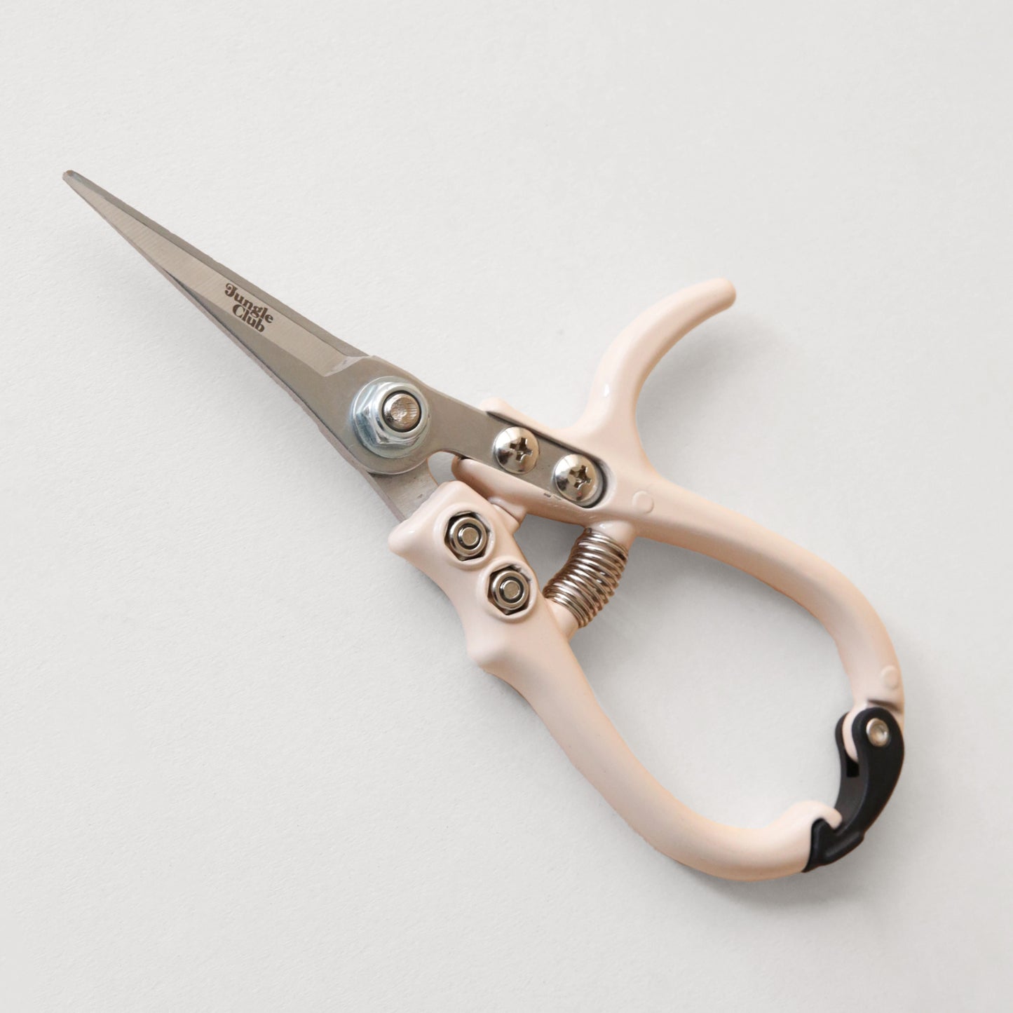 Pruning shears with a narrow tip, and light cream colored handle and a black clasp to connect when shears are not in use. There is small black text on the side of the shears that read, "Jungle Club".