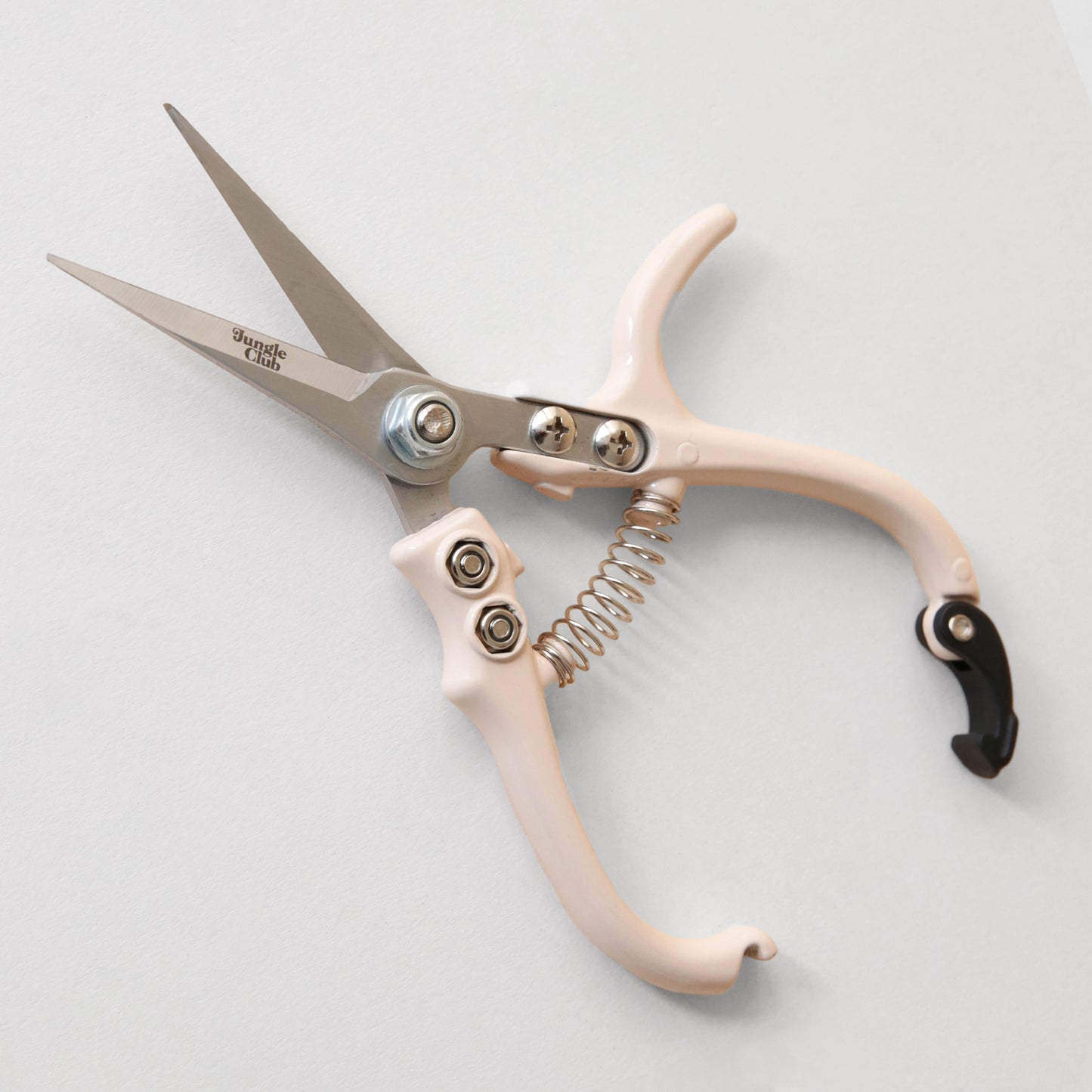Pruning shears with a narrow tip, and light cream colored handle and a black clasp to connect when shears are not in use. There is small black text on the side of the shears that read, "Jungle Club".