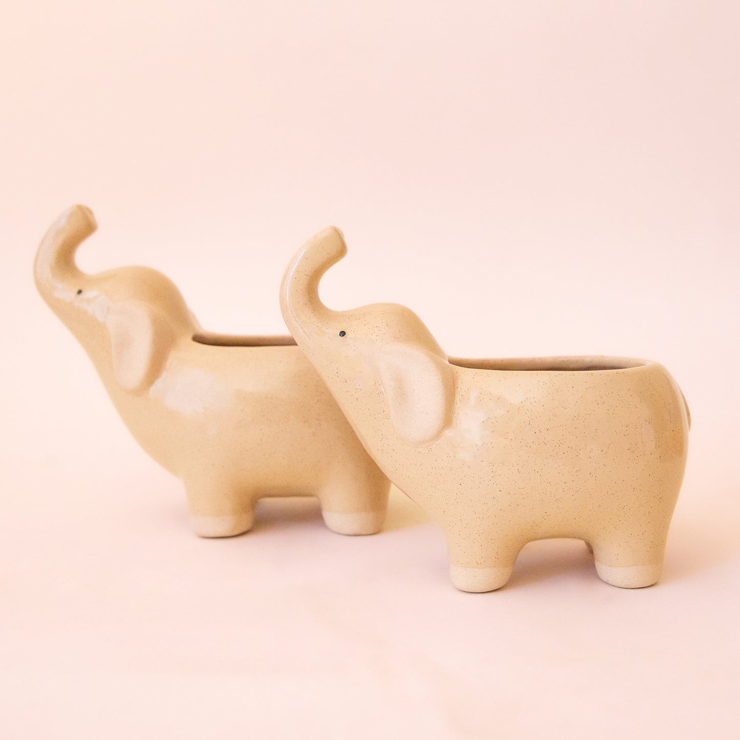 Two ceramic elephant with its nose in the air.  The ceramic is a tan color with speckles.