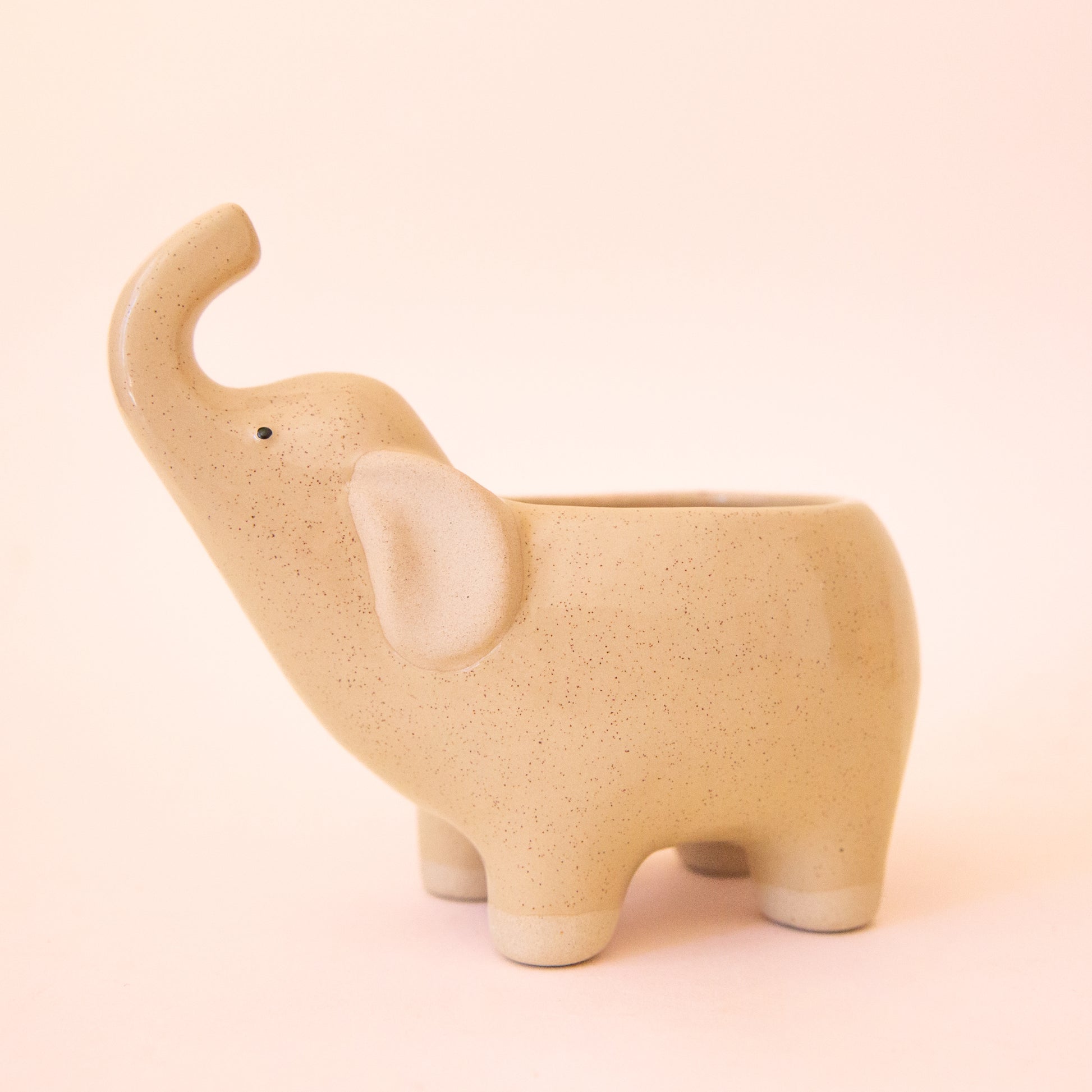A ceramic elephant with its nose in the air.  The ceramic is a tan color with speckles.