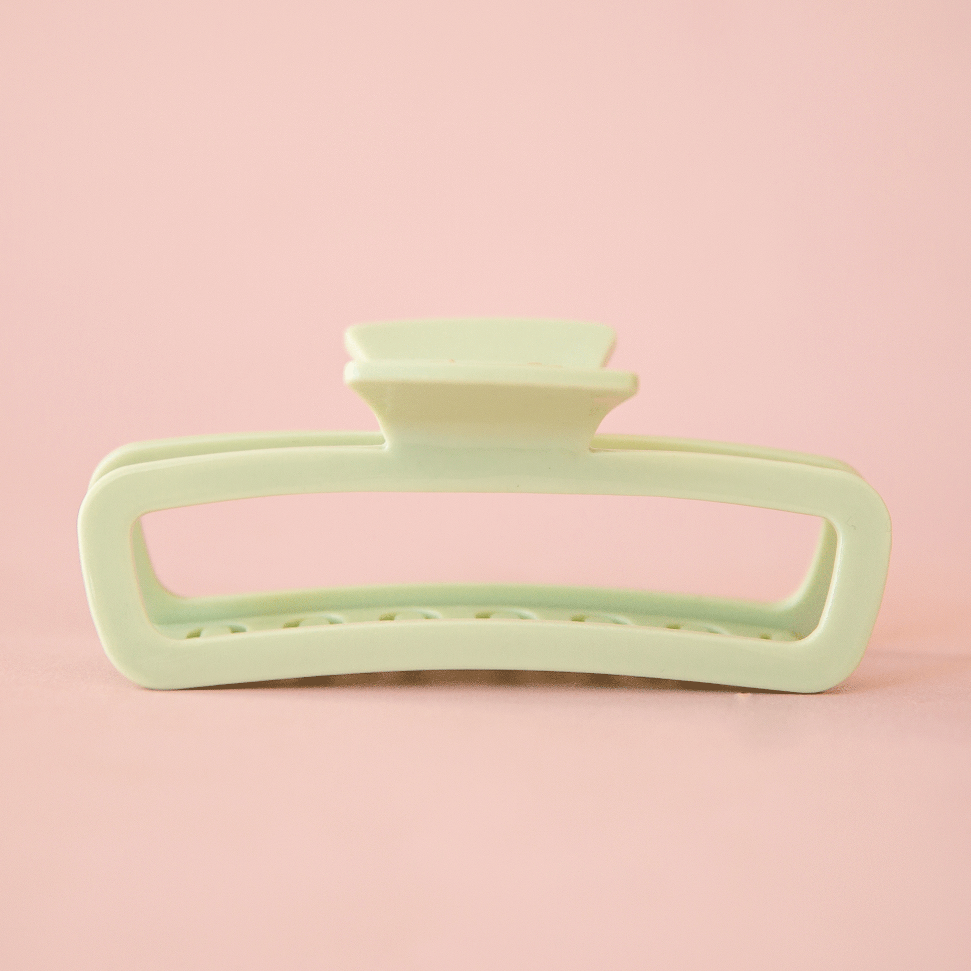 On a pink background is a rounded rectangle hair claw clip in mint green shade. 