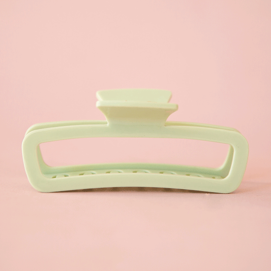 On a pink background is a rounded rectangle hair claw clip in mint green shade. 