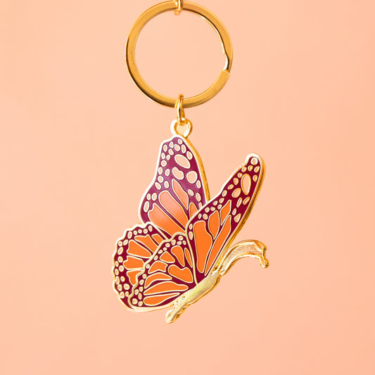 A pink and orange enamel butterfly shaped keychain with gold details. 
