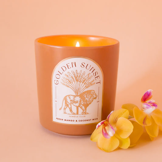 An orange candle with an arched label with a lion graphic and text above that reads, 'Golden Sunset'. 