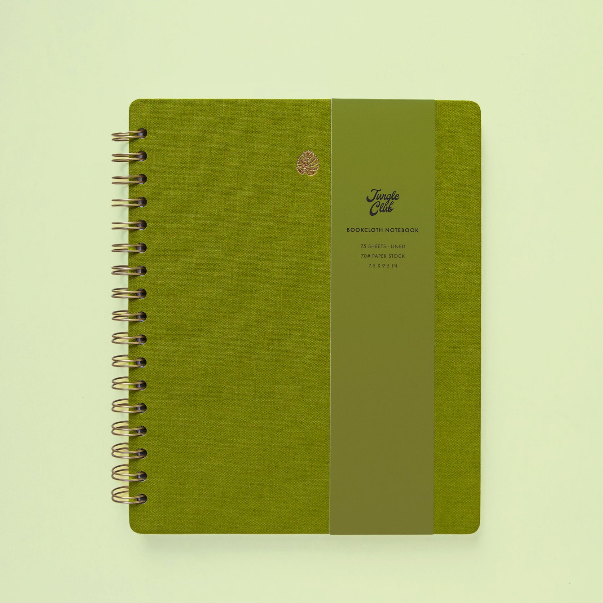 A green journal with a gold monstera leaf printed on it sits on a green background and leaves