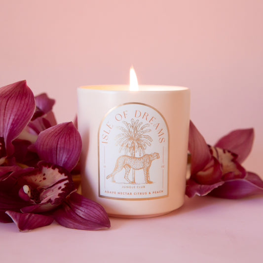 A neutral candle with an arched label with a cheetah and palm tree graphic and text that reads, 'Isle of Dreams'. 