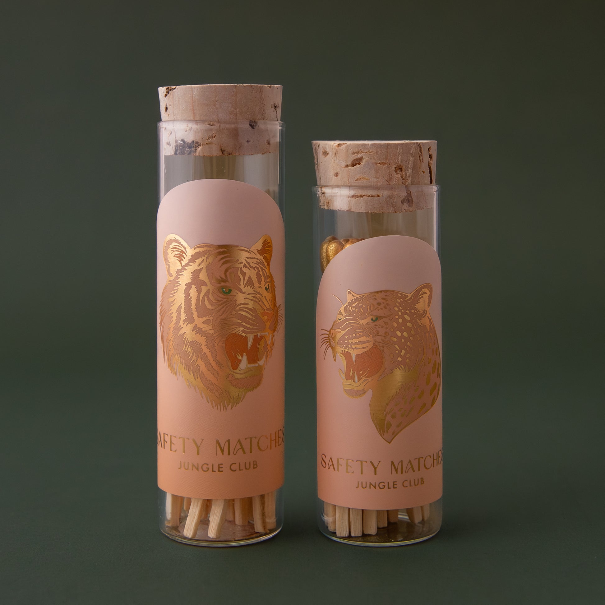Two clear glass vials with a cork lid that contains wooden safety matches. The label on one of the vials has a gold foil leopard on it and the other is a gold foil tiger. 