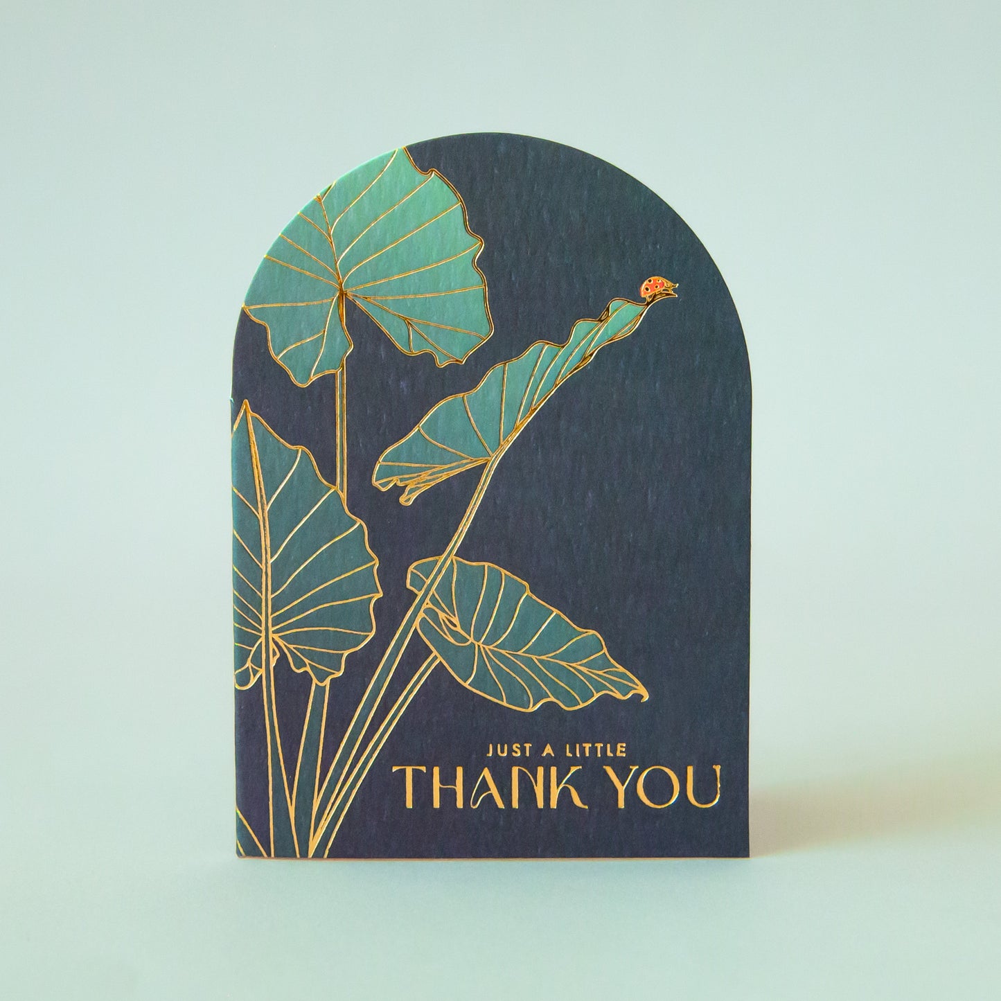An arched dark teal card with gold foiled text that reads, 'Just a Little Thank You'. 
