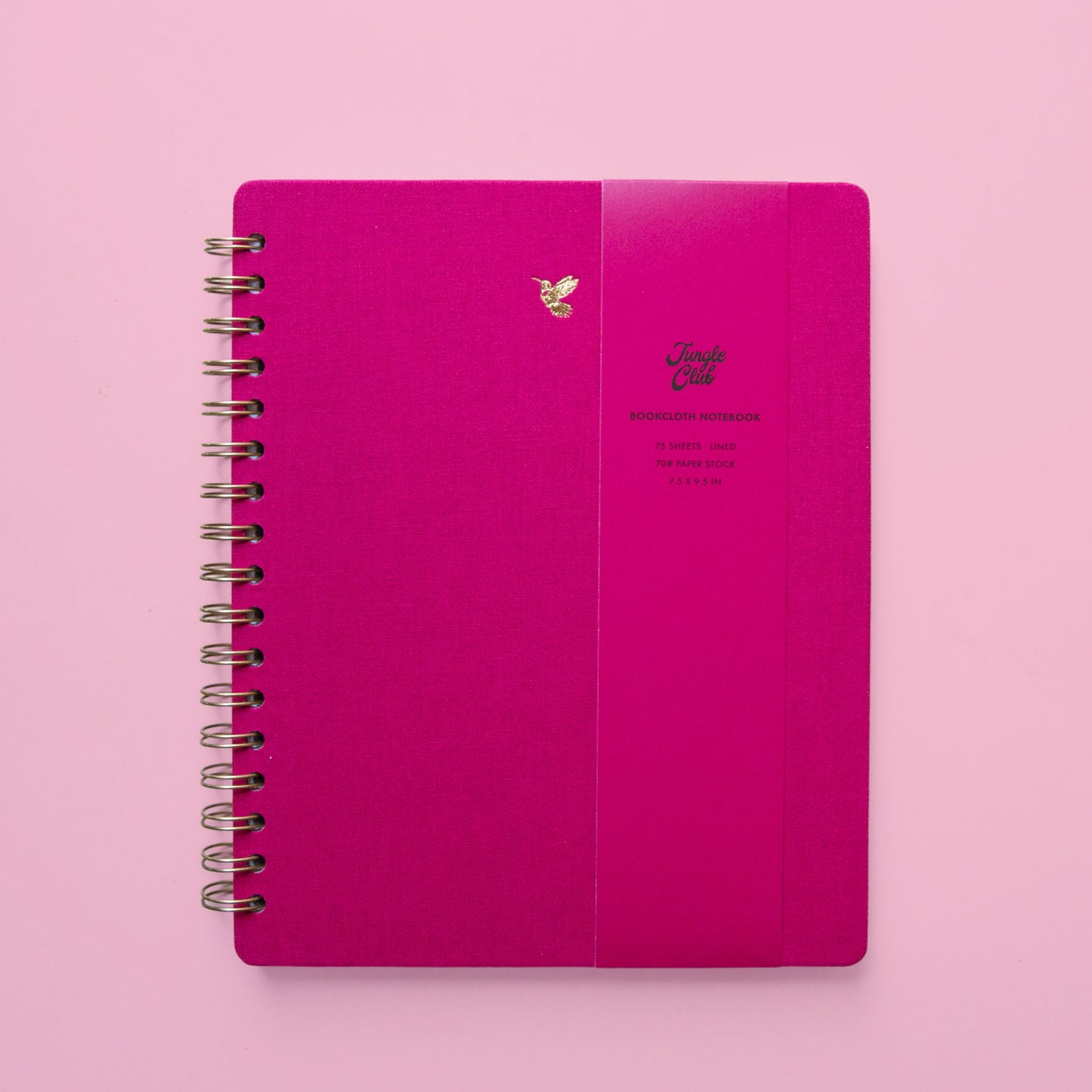 A hot pink spiral bound notebook with a gold foiled hummingbird graphic in the top center. 