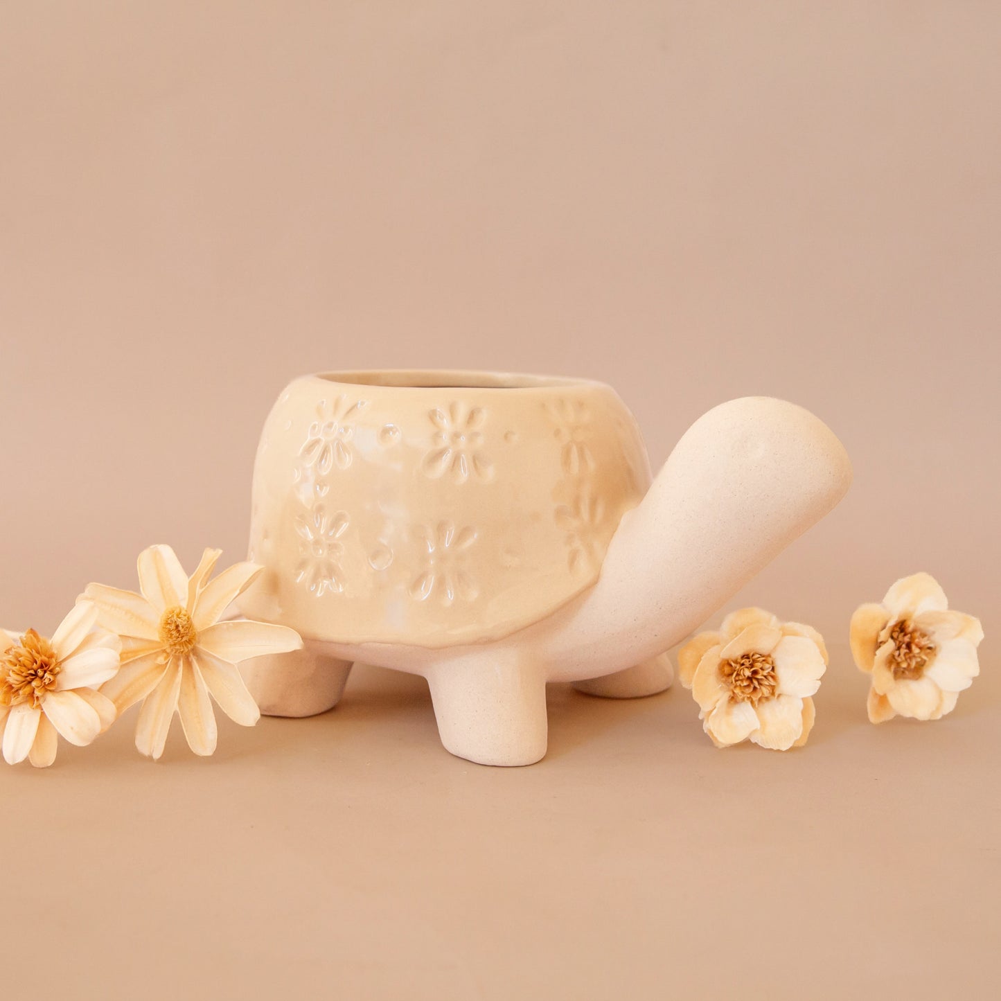 a ceramic planter in the shape of a turtle with a light tan "shell" with a subtle floral print. 