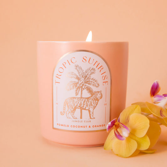 A light peach colored candle with a tiger and palm tree graphic and text above that reads, 'Tropic Sunrise'. 
