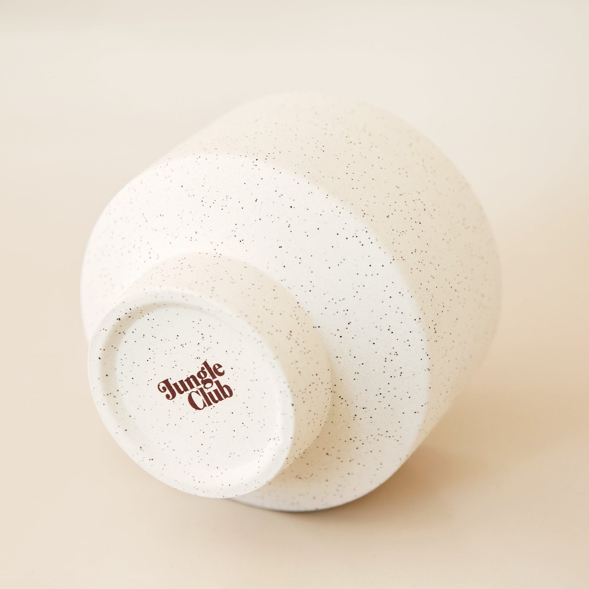 Bottom view of ivory speckled pot. The bottom of the pot reads 'jungle club' in a rust color.